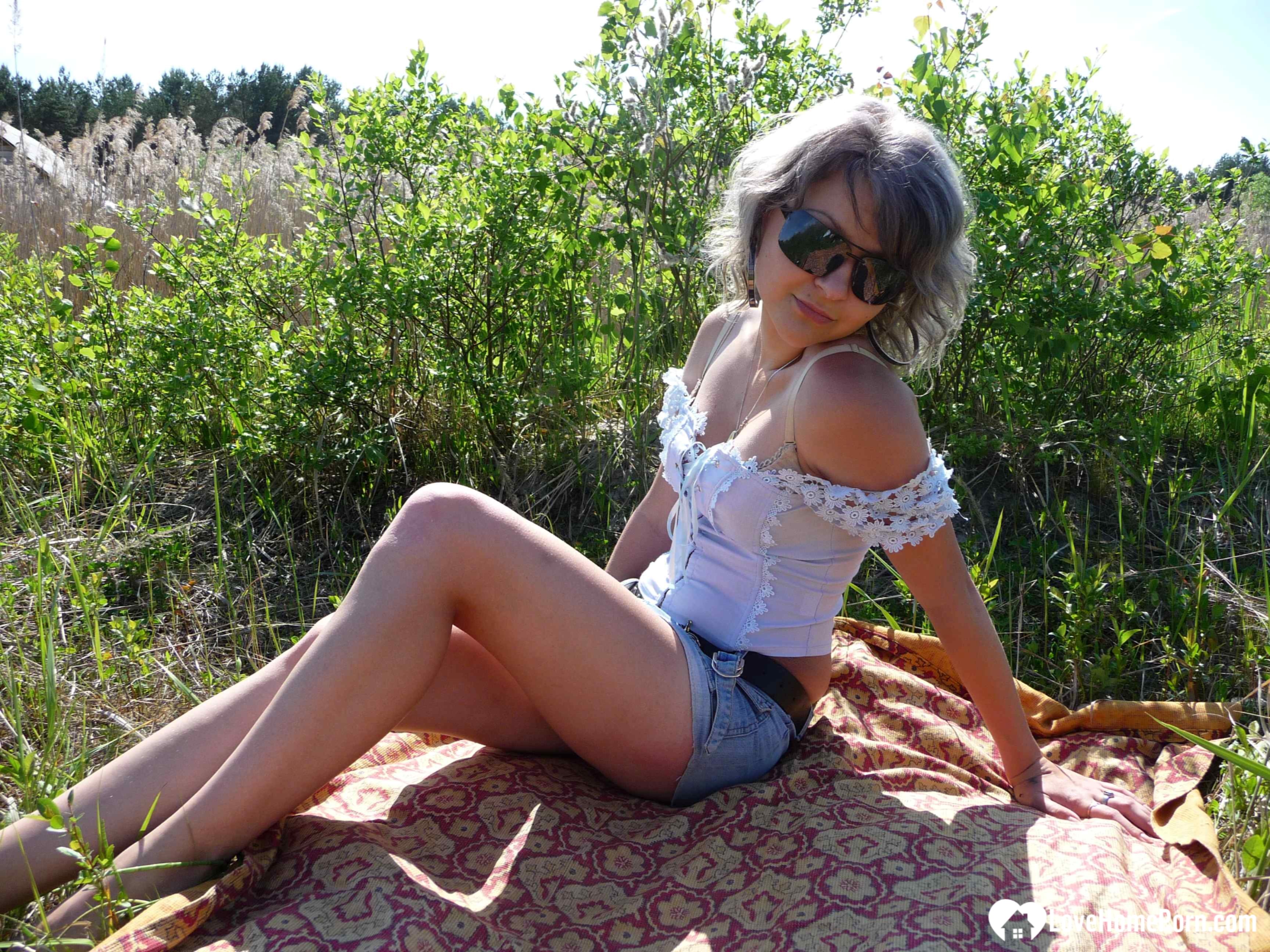 Gray-haired beauty posing naked outdoors on a blanket