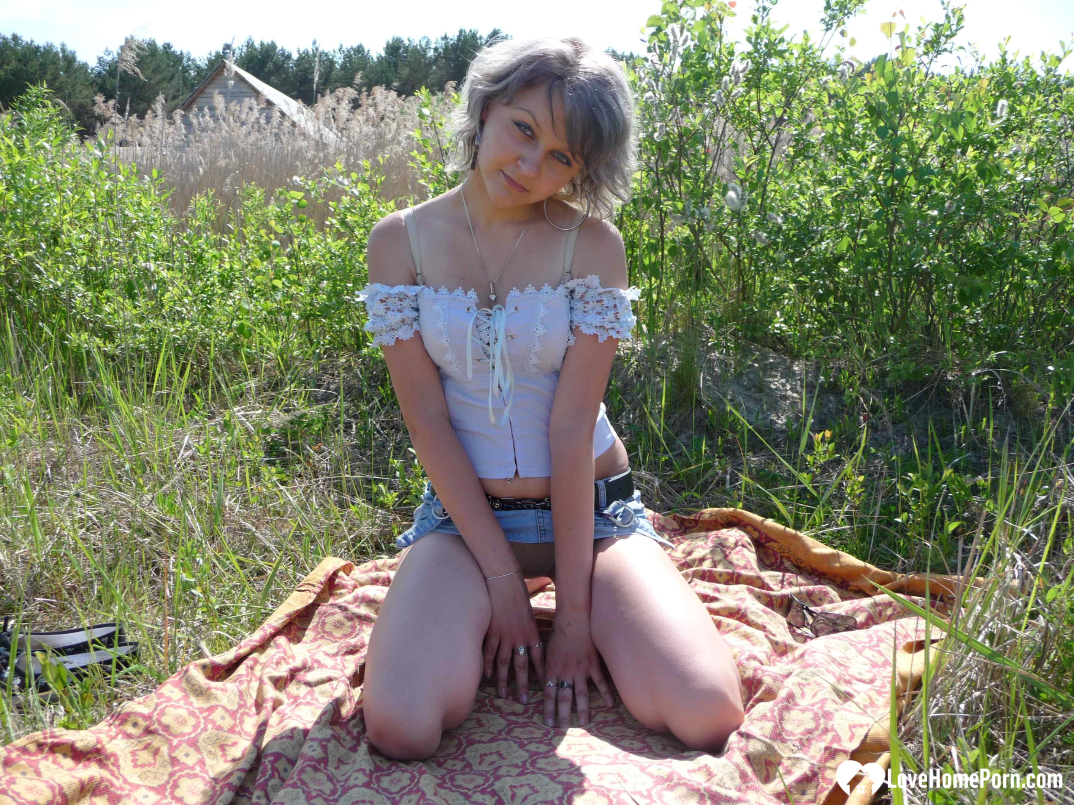 Gray-haired beauty posing naked outdoors on a blanket
